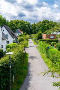 Peaceful suburban street lined with green hedges and houses under a partly cloudy sky.